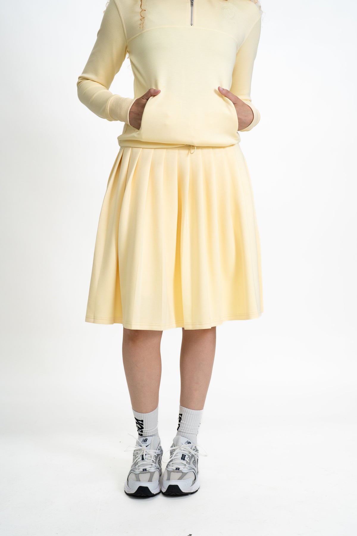 Person wearing a light yellow outfit with a skirt on a white background