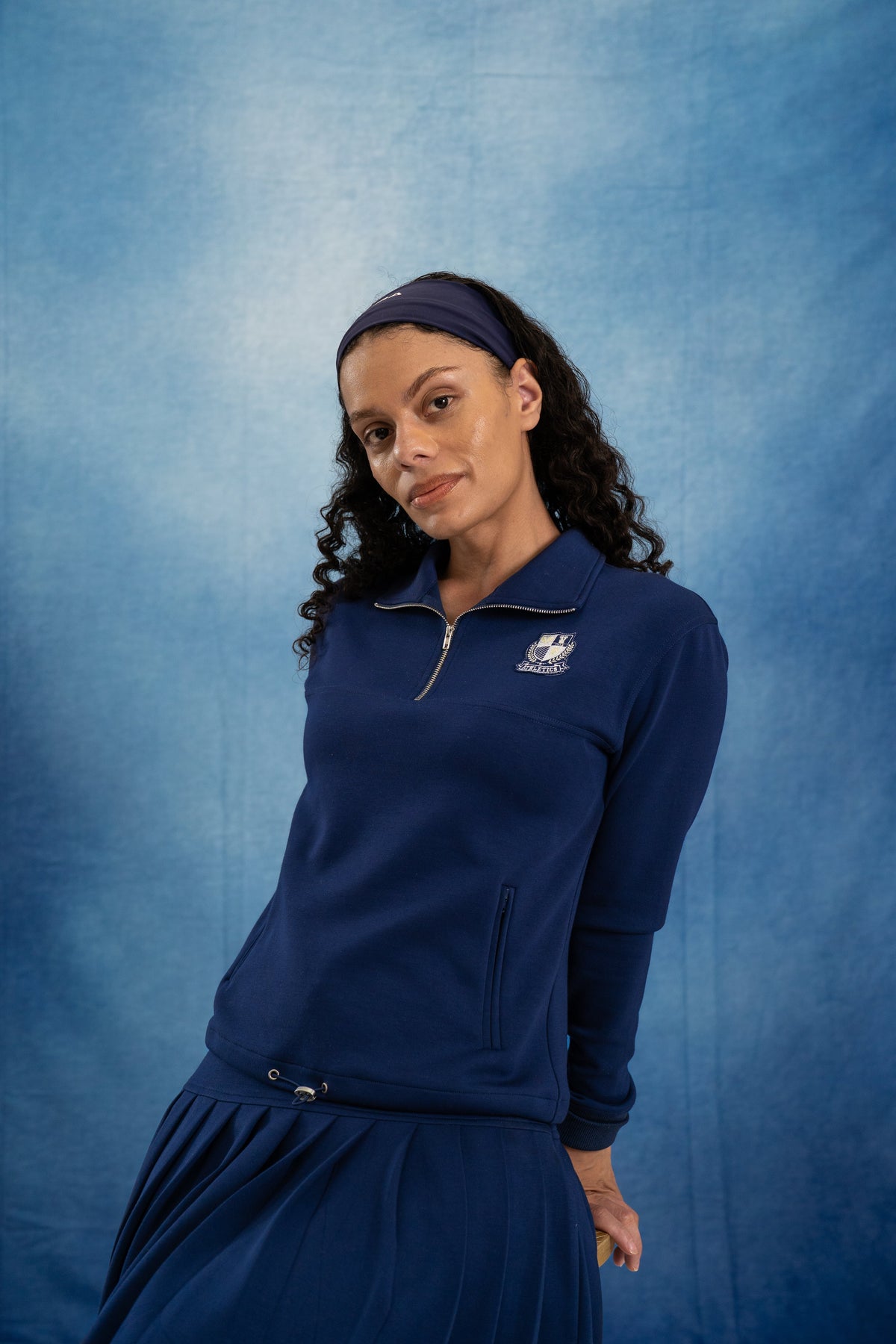 Woman wearing a navy blue outfit with a logo against a matching blue background